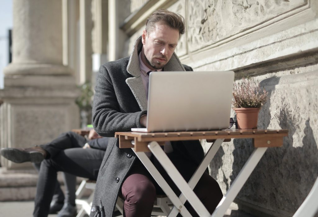 Vyras naudojasi kompiuteriu lauko kavinėje. Andrea Piacquadio nuotr. / Pexels.com