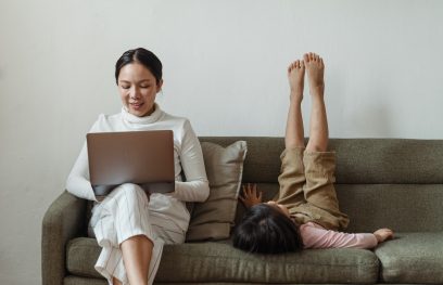 Moteris su kompiuteriu ant kelių ir šalia gulinčiu vaiku / Pexels nuotr.