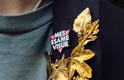 Į švarko atlapą įsegtas ženkliukas „MES ESAME VISUR“