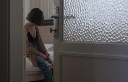 Liūdna moteris sėdi miegamajame, veidą dengia plaukai