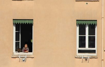 daugiabučio namo langai, pro vieną jų žiūri moteris