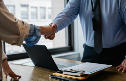 moteris ir vyras spaudžia vienas kitam ranką biure