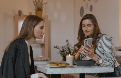 dvi moterys bendrauja prie stalo, viena rodo kitai telefoną